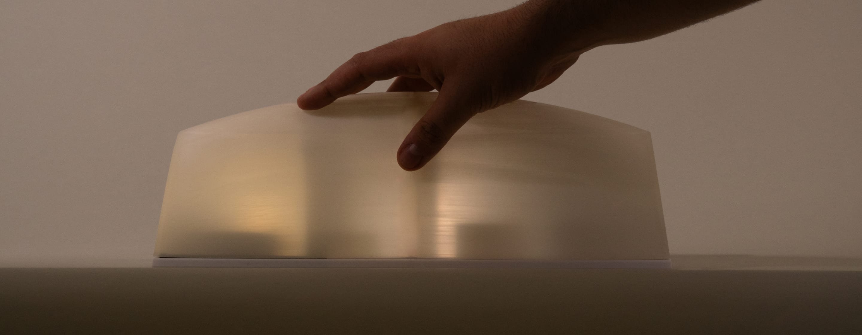 Une main posée sur la cloche translucide du plateau, dans une lumière chaude